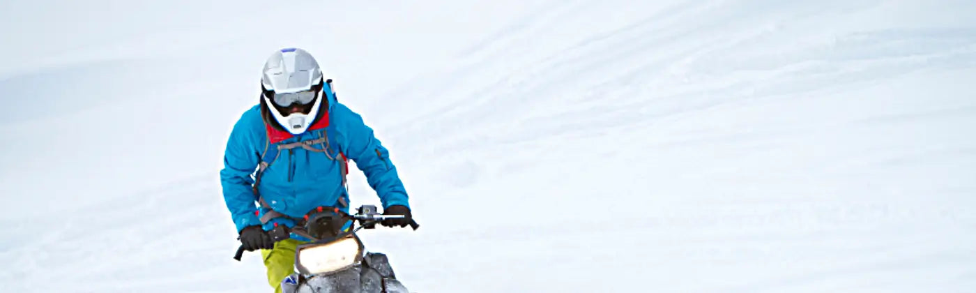 Person with winter suite riding a snowmobile in a snowy mountain