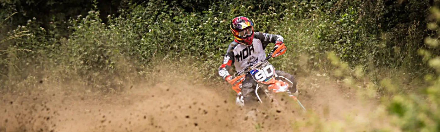 Person with motor bike suite riding a dirt bike drifting in a dirt in a forest